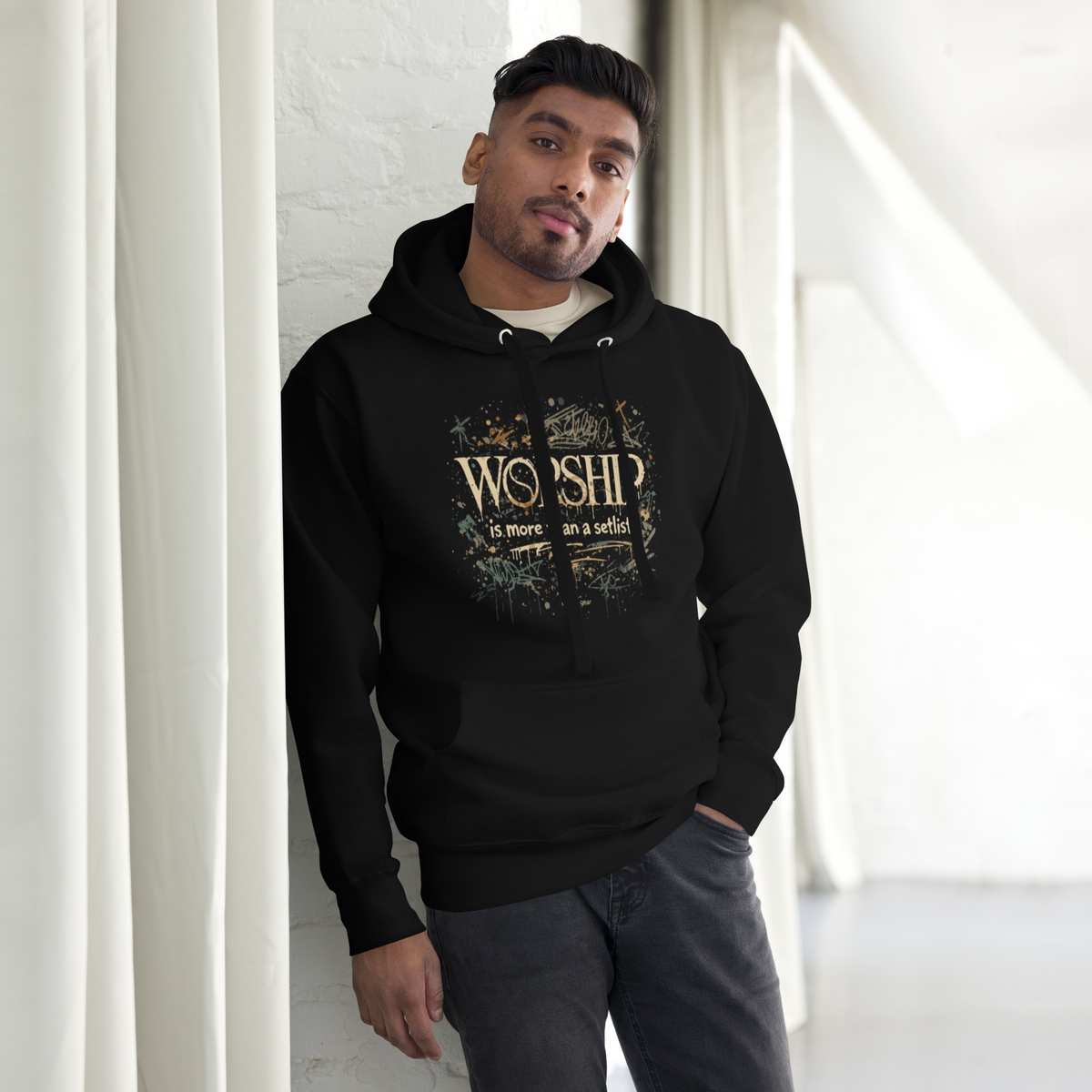 Man wearing the black Worship Is More Than a Setlist hoodie, leaning on a white wall